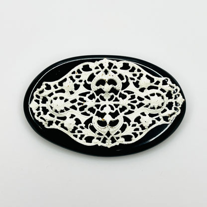 Vintage 1950s oval brooch with ornate white enamel floral filigree over a glossy black base