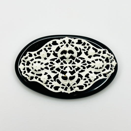 Vintage 1950s oval brooch with ornate white enamel floral filigree over a glossy black base