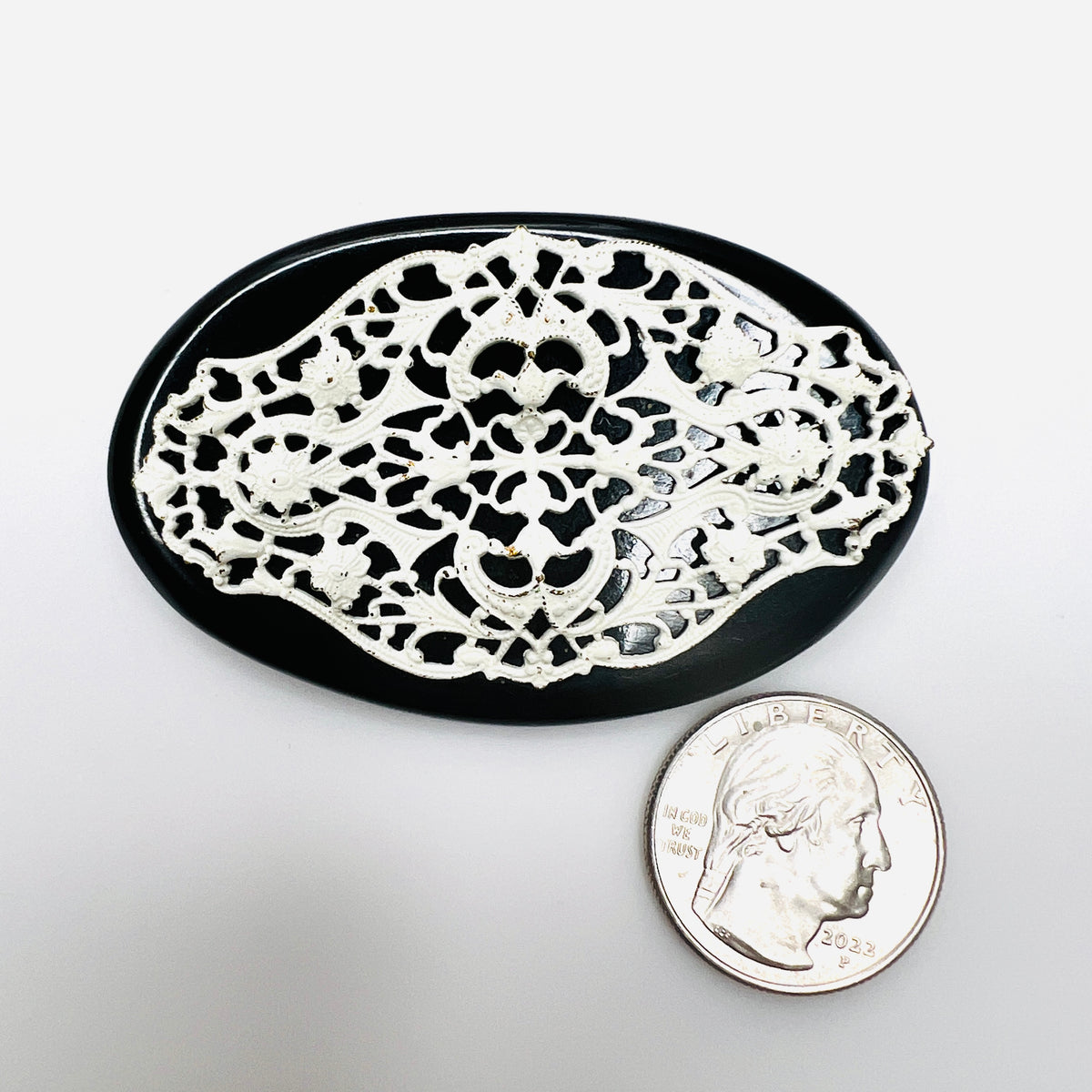 Black and white vintage filigree brooch beside quarter showing oval shape and size