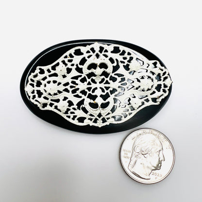 Black and white vintage filigree brooch beside quarter showing oval shape and size