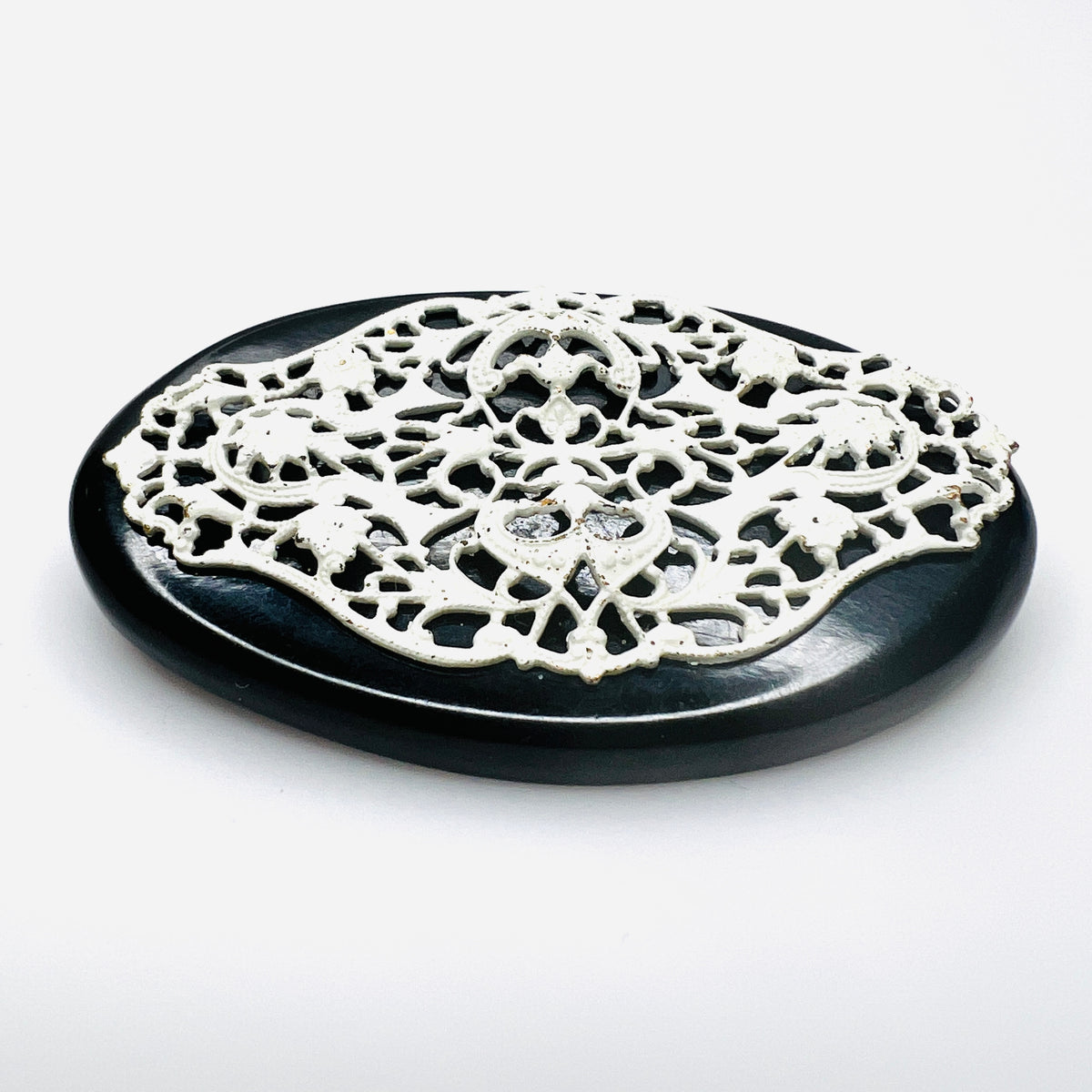 Side view of 1950s enamel brooch showing raised white metal filigree on black base