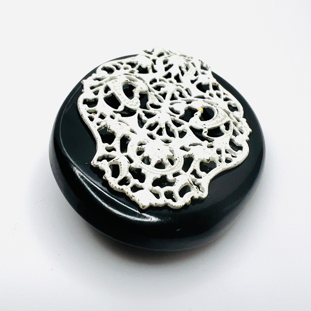 Angled view of 1950s enamel brooch showing raised white metal filigree on black base