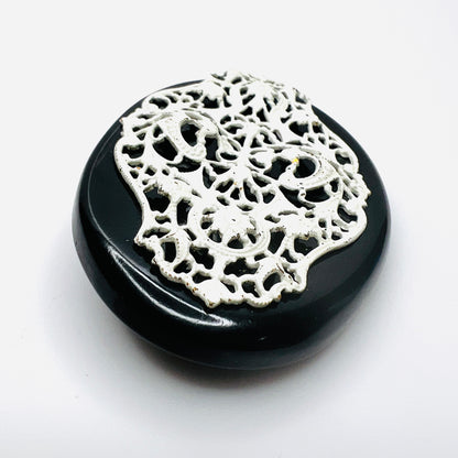 Angled view of 1950s enamel brooch showing raised white metal filigree on black base