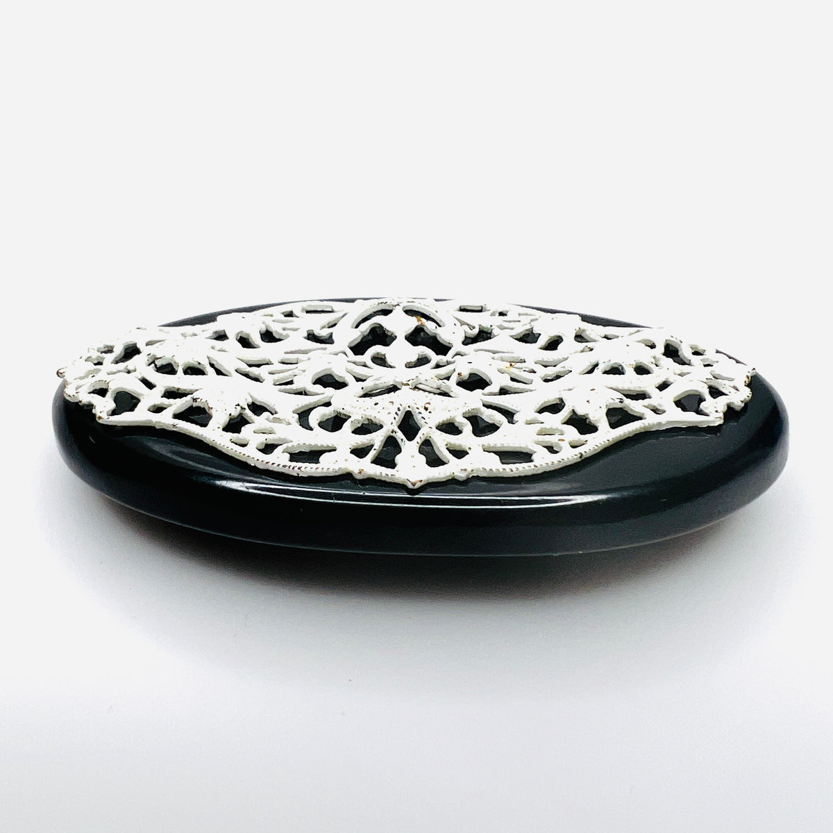 Side view of 1950s enamel brooch showing raised white metal filigree on black base