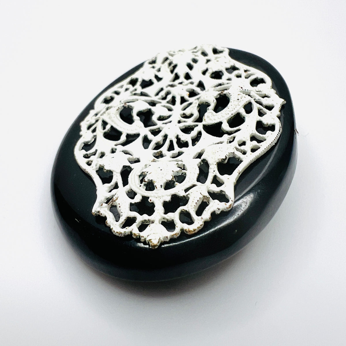 Angled view of 1950s enamel brooch showing raised white metal filigree on black base