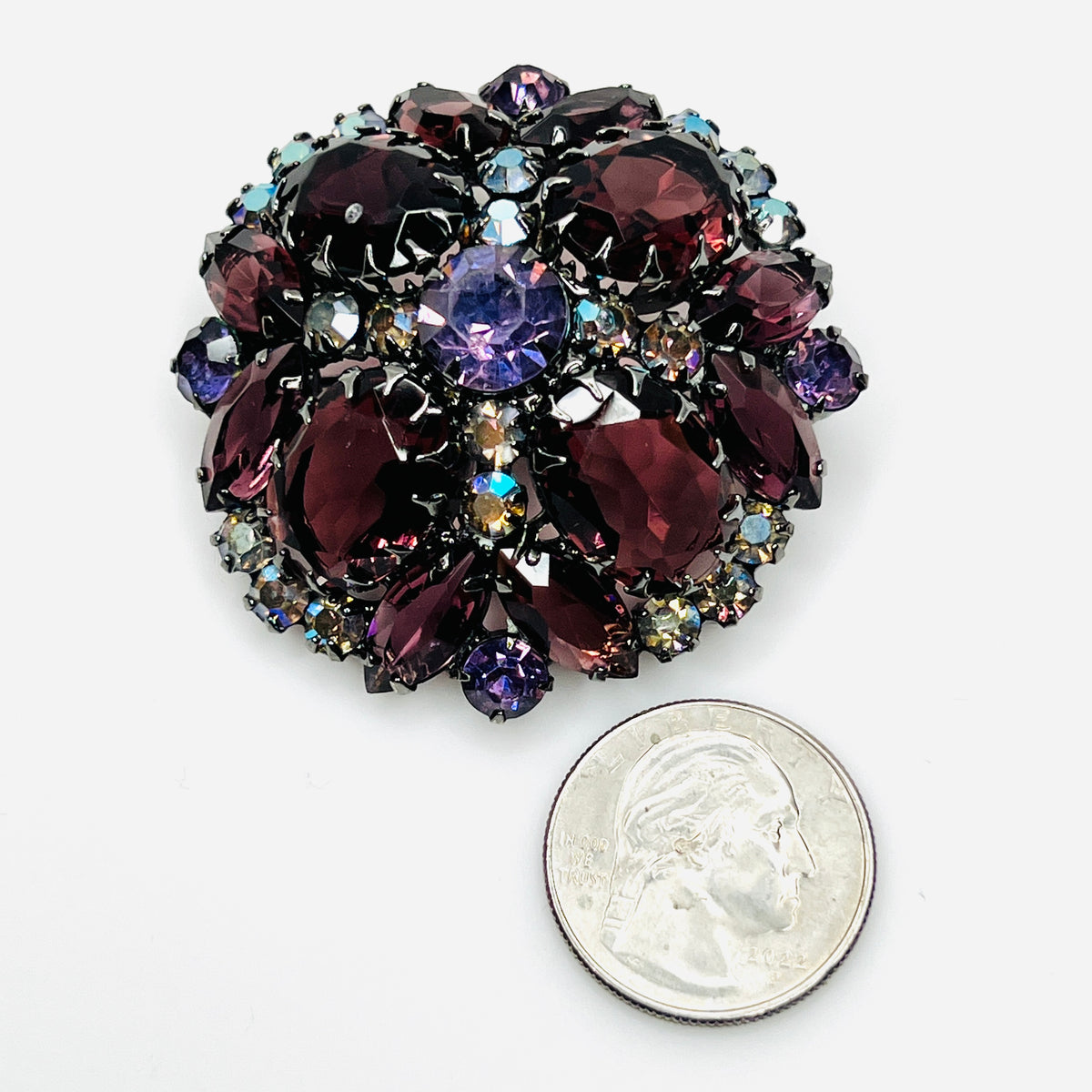 Purple and wine rhinestone Juliana brooch beside a quarter, showing its 2-inch size and layered design.