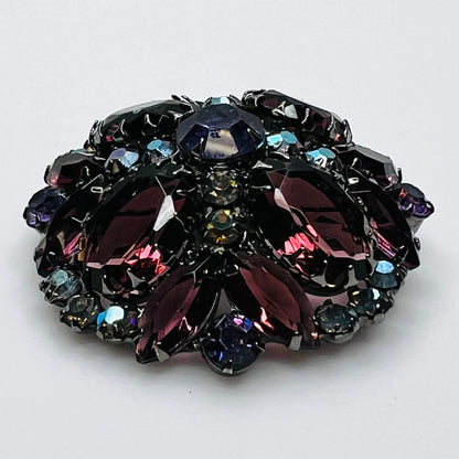 Angled view of Juliana rhinestone brooch showing the raised dome, purple glass stones, and iridescent accents.