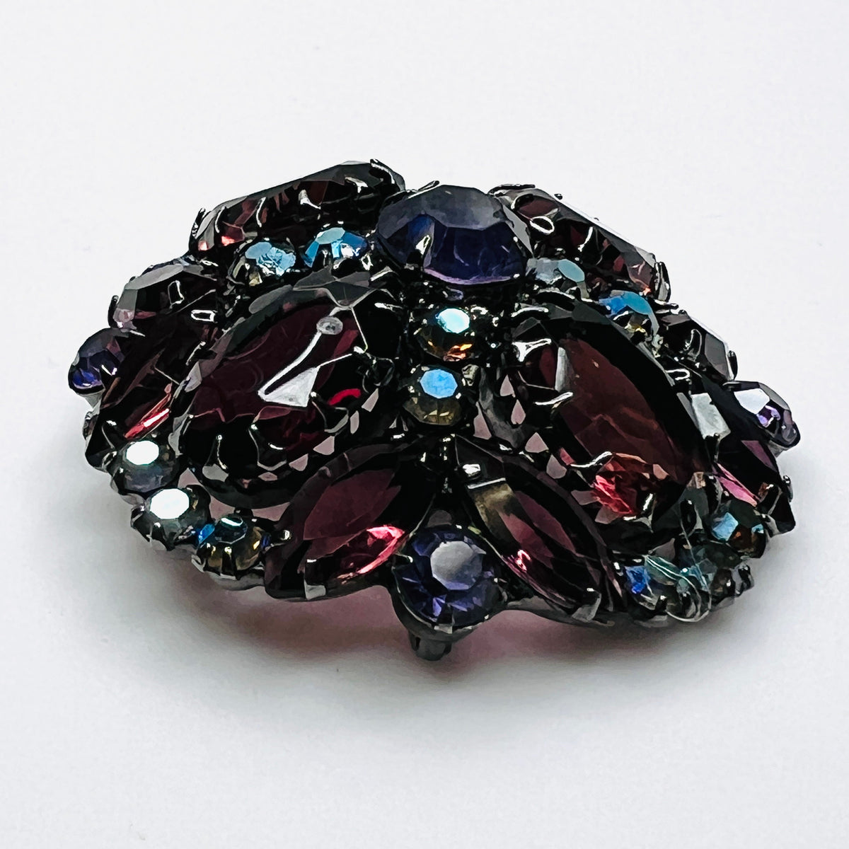 Angled view of Juliana rhinestone brooch showing the raised dome, purple glass stones, and iridescent accents.