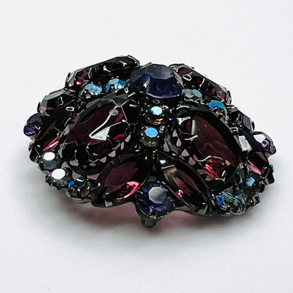 Angled view of Juliana rhinestone brooch showing the raised dome, purple glass stones, and iridescent accents.