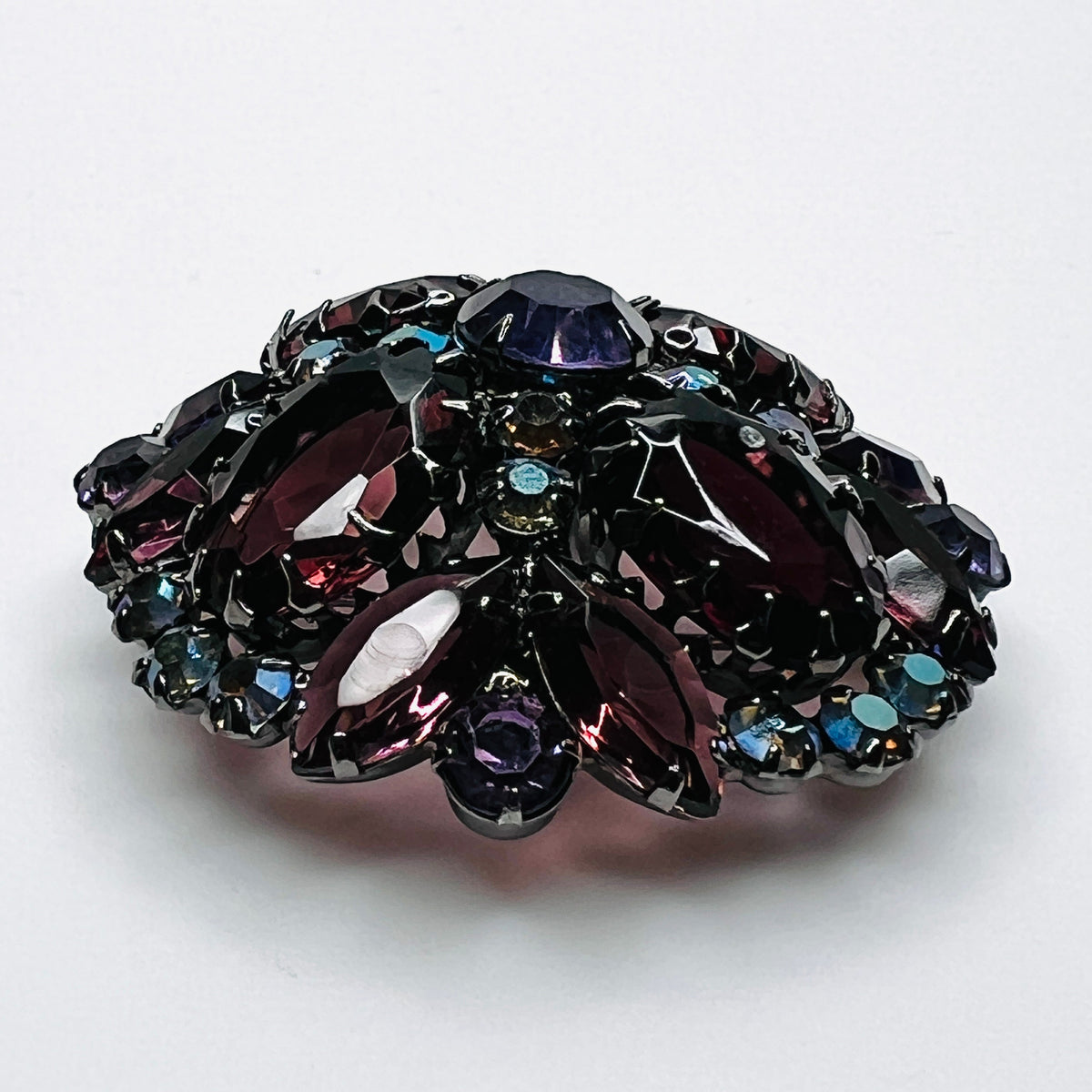 Angled view of Juliana rhinestone brooch showing the raised dome, purple glass stones, and iridescent accents.