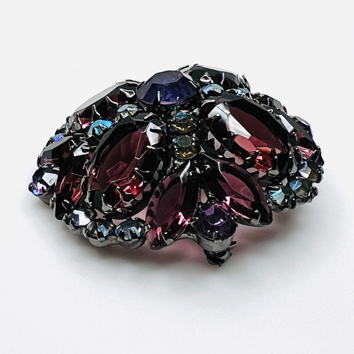 Angled view of Juliana rhinestone brooch showing the raised dome, purple glass stones, and iridescent accents.