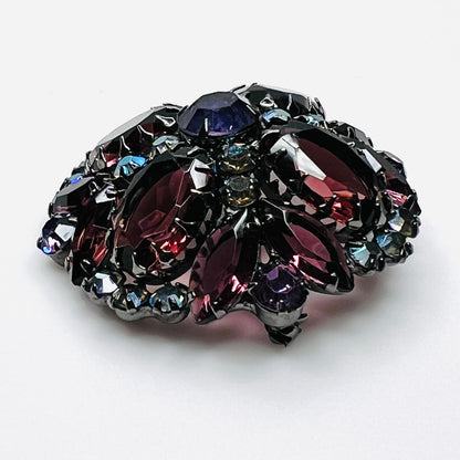 Angled view of Juliana rhinestone brooch showing the raised dome, purple glass stones, and iridescent accents.