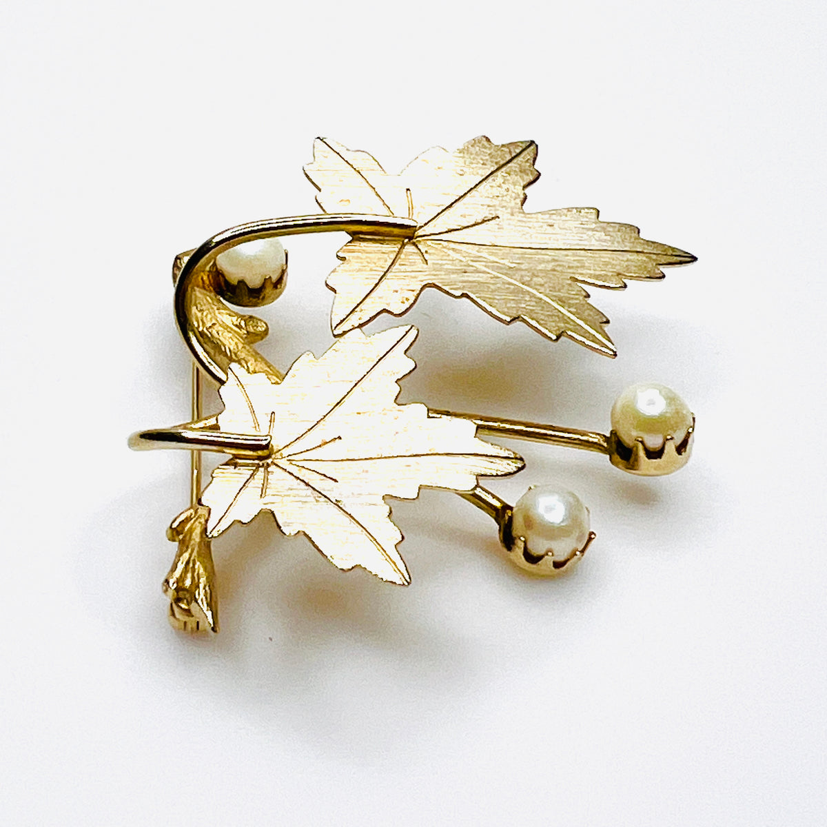 Angled view of vintage gold tone maple leaf brooch with curved stems and cultured pearls