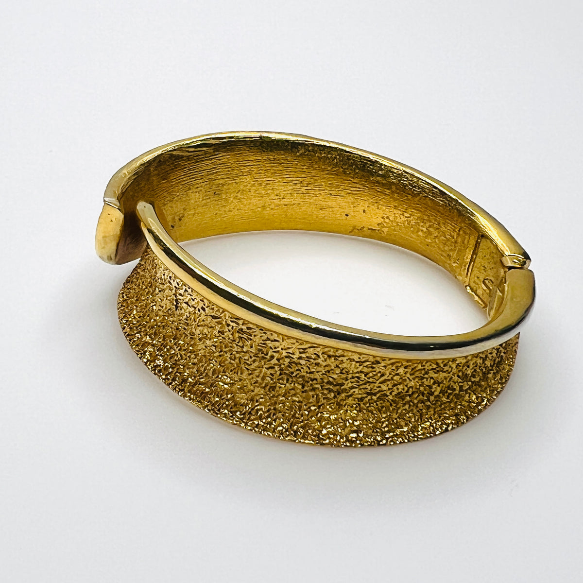 Side view of Vintage Trifari textured gold tone hinged bracelet with sweeping polished edge