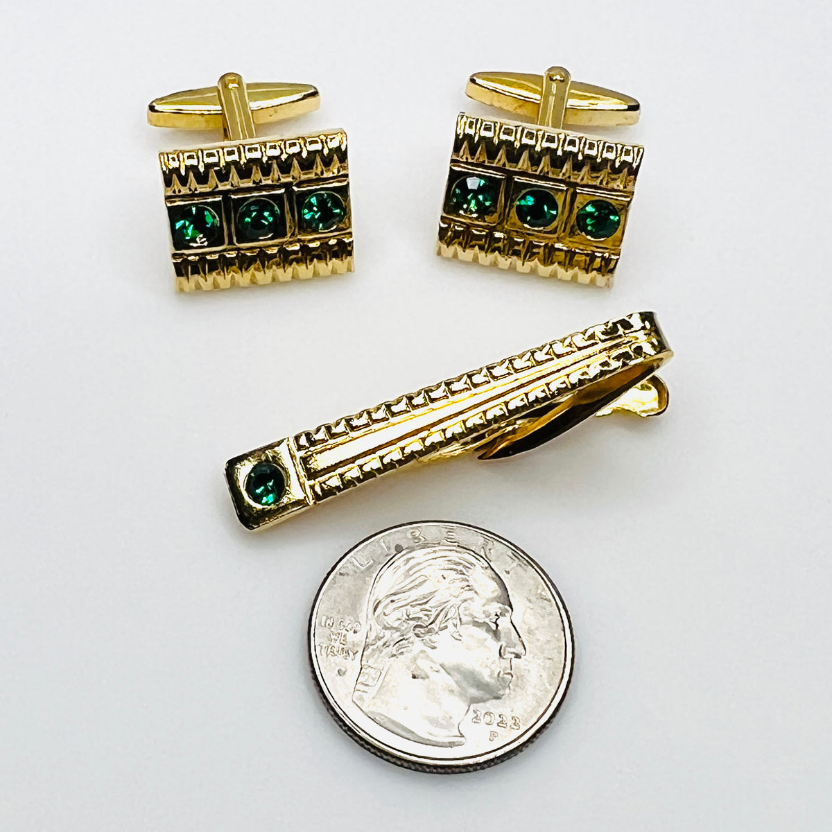 Vintage 1960s green rhinestone cufflinks and matching gold tone tie clip beside quarter
