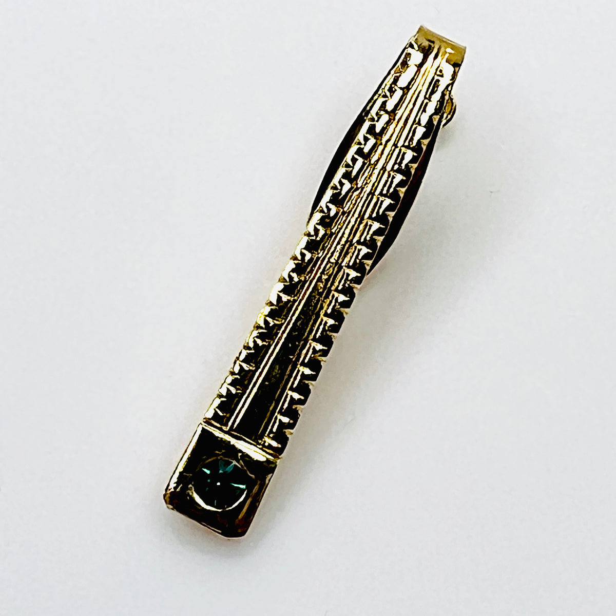 Close-up of gold tone vintage tie clip with emerald green rhinestone and textured geometric design