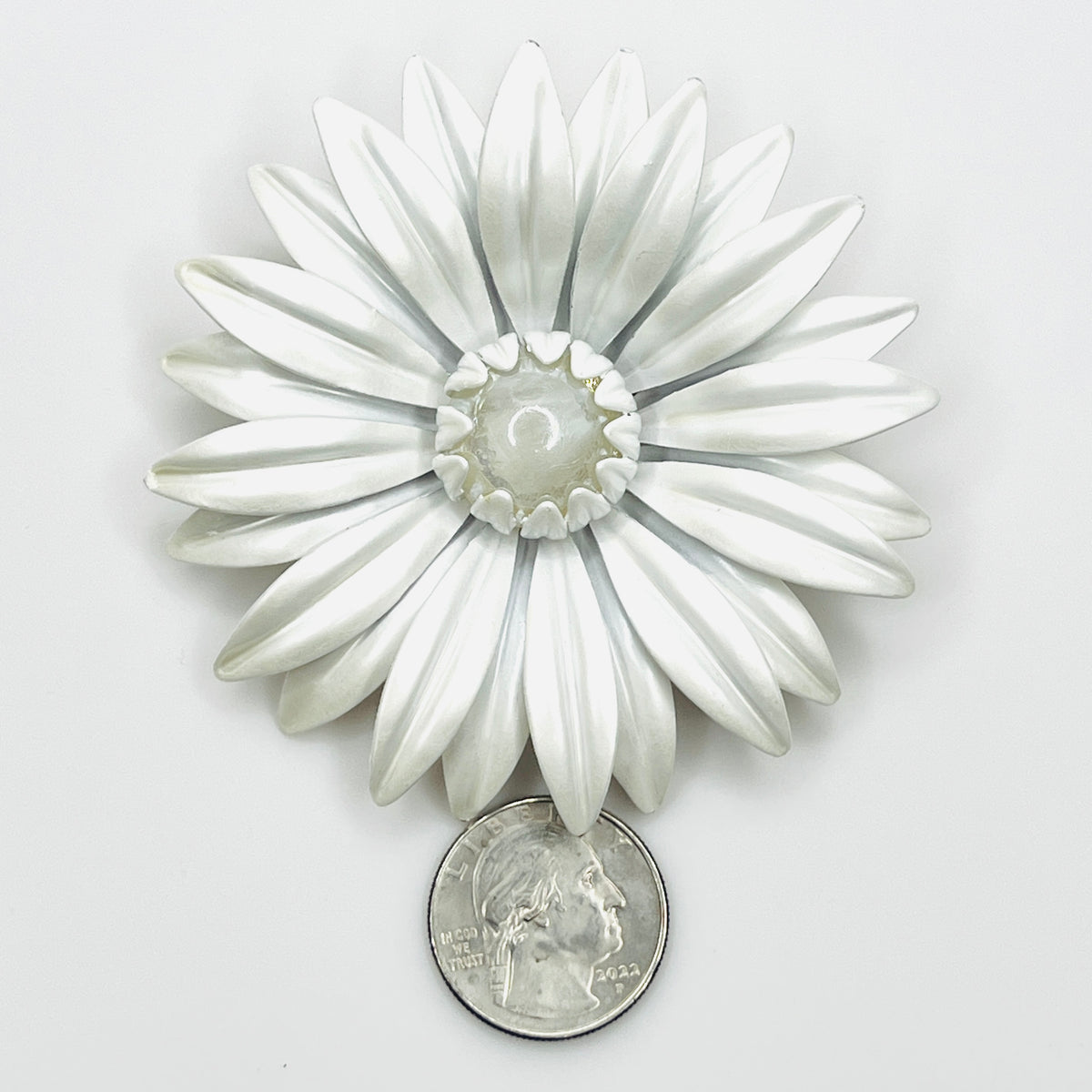 White enamel daisy brooch beside a quarter, showing its 3-inch size and layered flower design.