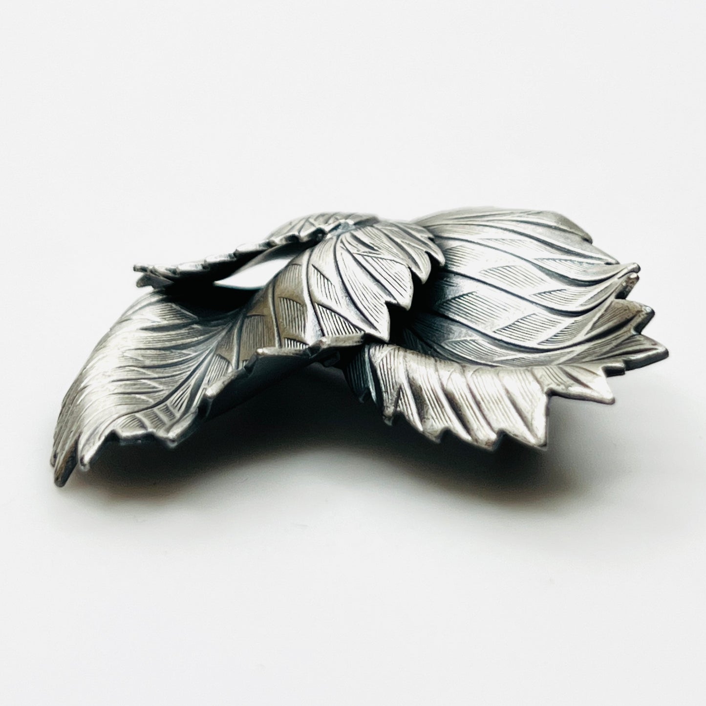 Side profile of vintage sculptural three leaf brooch in aged silver tone