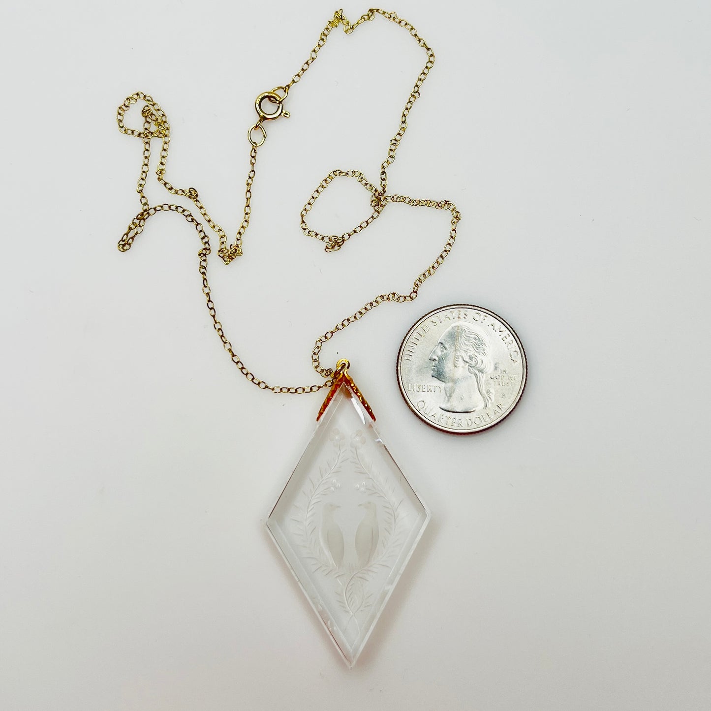 Close-up of crystal love birds pendant next to coin for scale