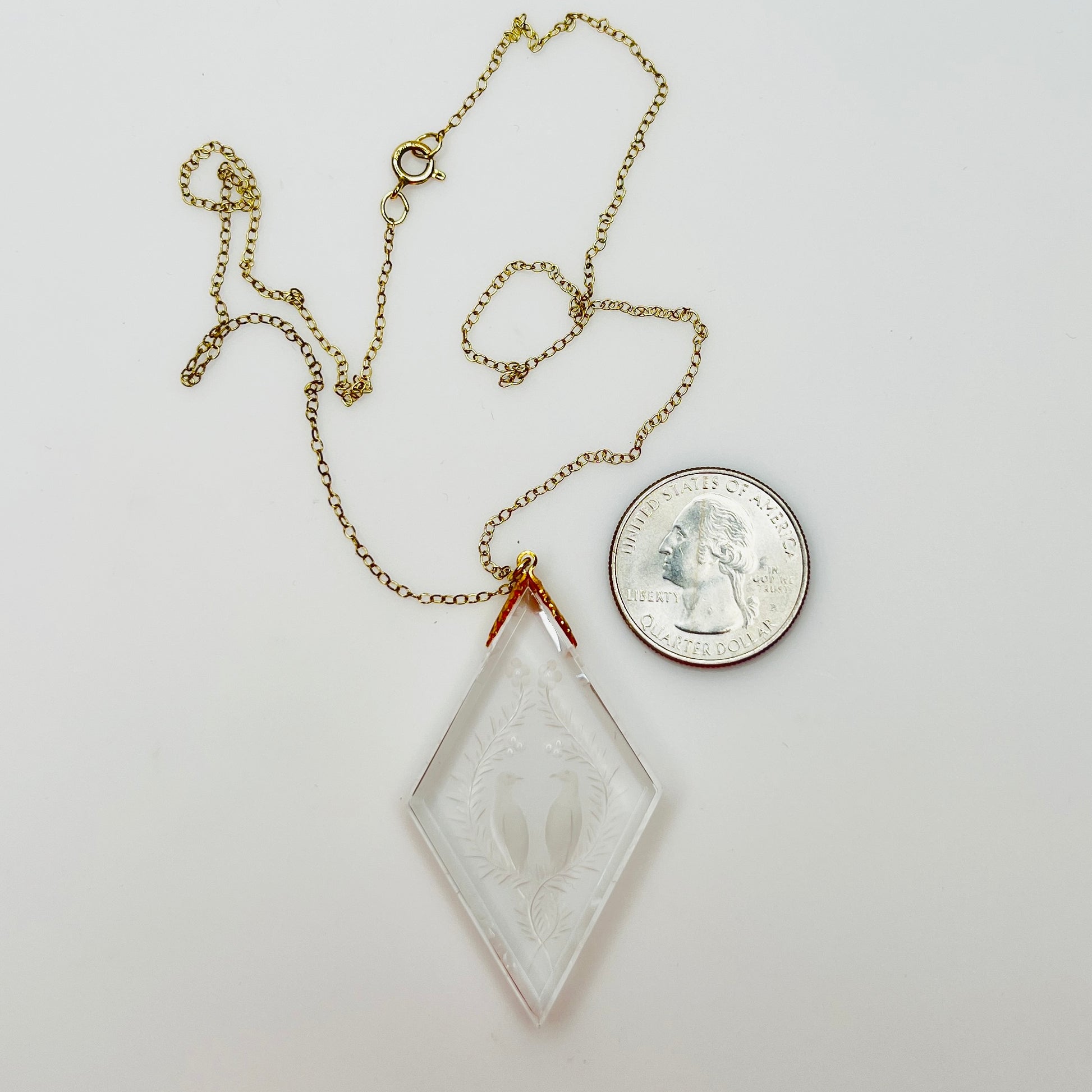 Close-up of crystal love birds pendant next to coin for scale