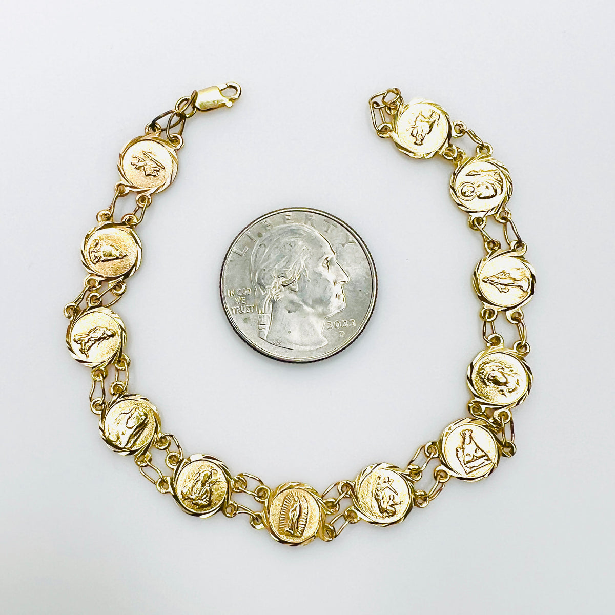 14K gold religious medal bracelet with Catholic saint panels beside quarter for scale