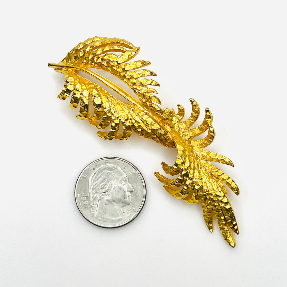 Vintage signed BSK gold-tone fern leaf brooch beside quarter showing elongated size and intricate openwork detailing