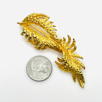 Vintage signed BSK gold-tone fern leaf brooch beside quarter showing elongated size and intricate openwork detailing