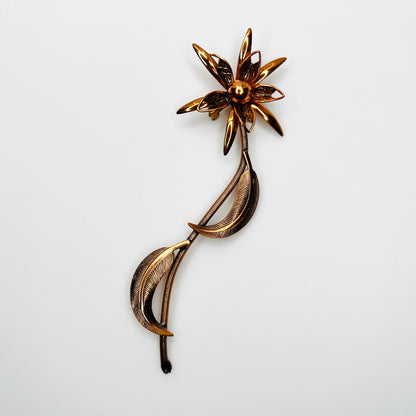Vintage 1970s copper-tone flower brooch with layered petals, long textured stem and curved leaves