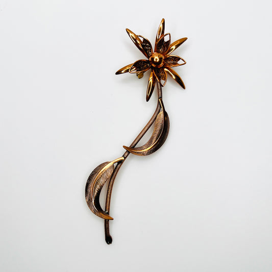 Vintage 1970s copper-tone flower brooch with layered petals, long textured stem and curved leaves