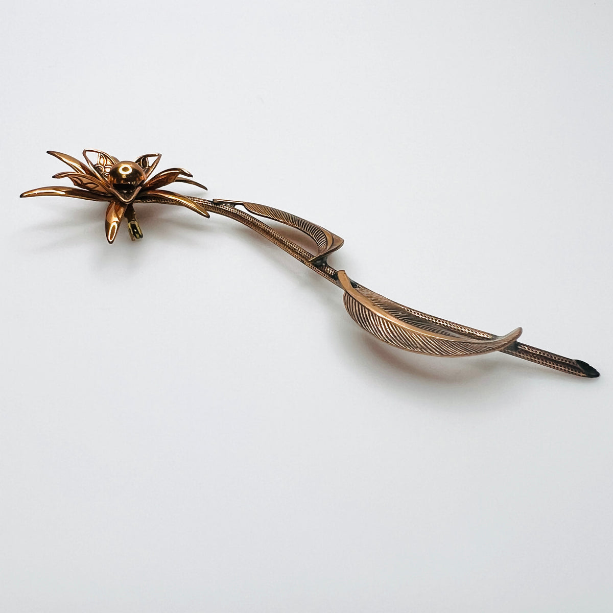 Side profile of vintage copper flower brooch showing raised petals and sculptural curved leaves