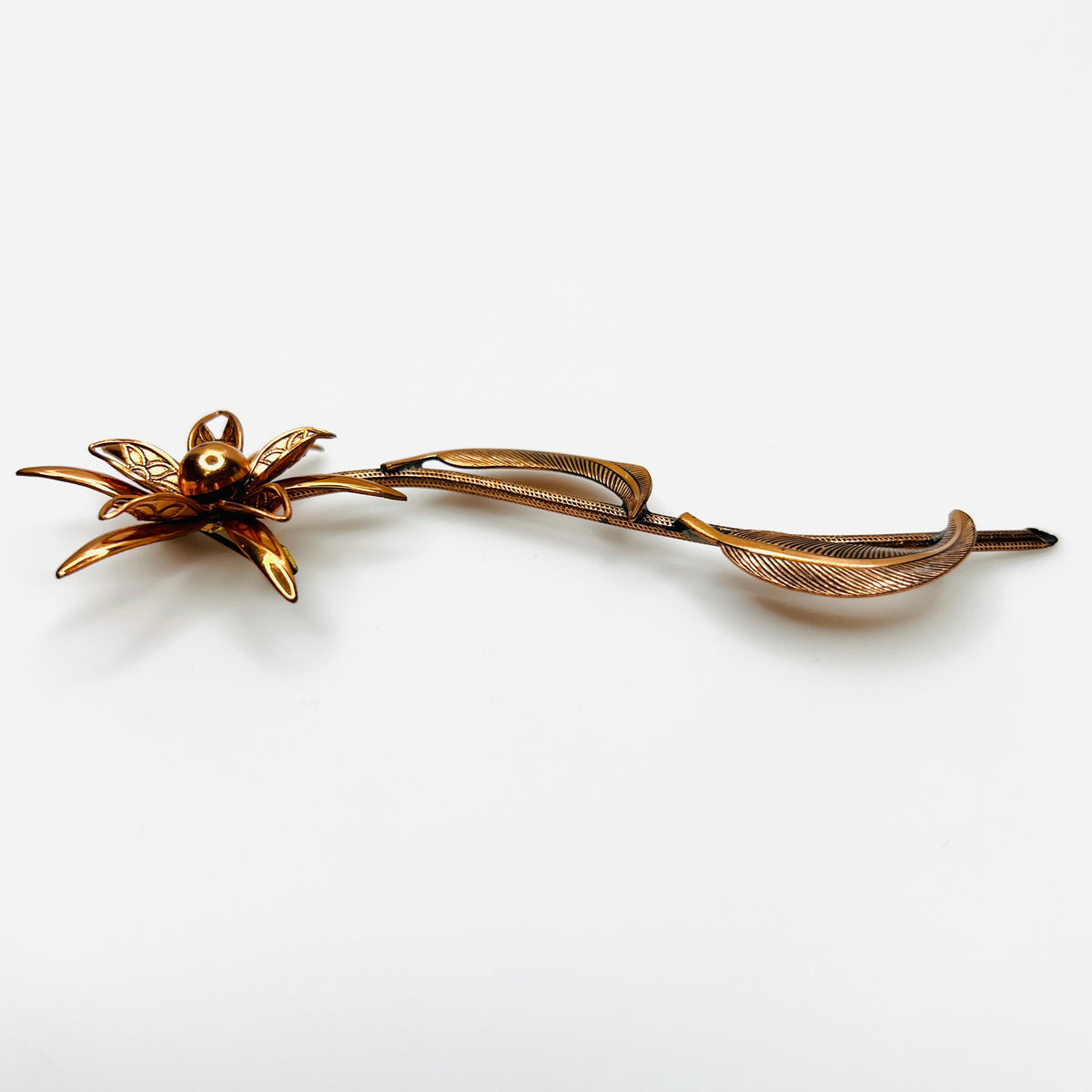 Side profile of vintage copper flower brooch showing raised petals and sculptural curved leaves