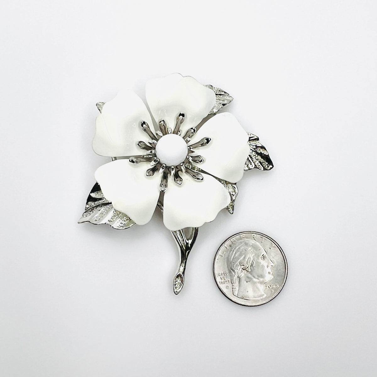 Large Sarah Coventry white enamel flower brooch shown beside quarter for scale