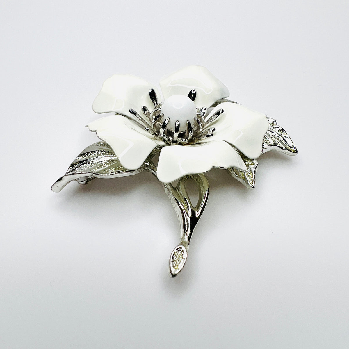 Side view of white enamel flower brooch showing dimensional petals, center and silver-tone leaves