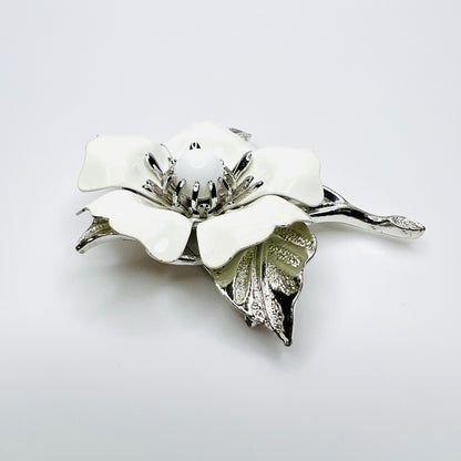 Side view of white enamel flower brooch showing dimensional petals, center and silver-tone leaves