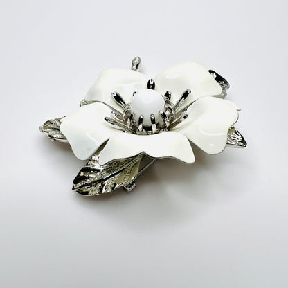 Side view of white enamel flower brooch showing dimensional petals, center and silver-tone leaves