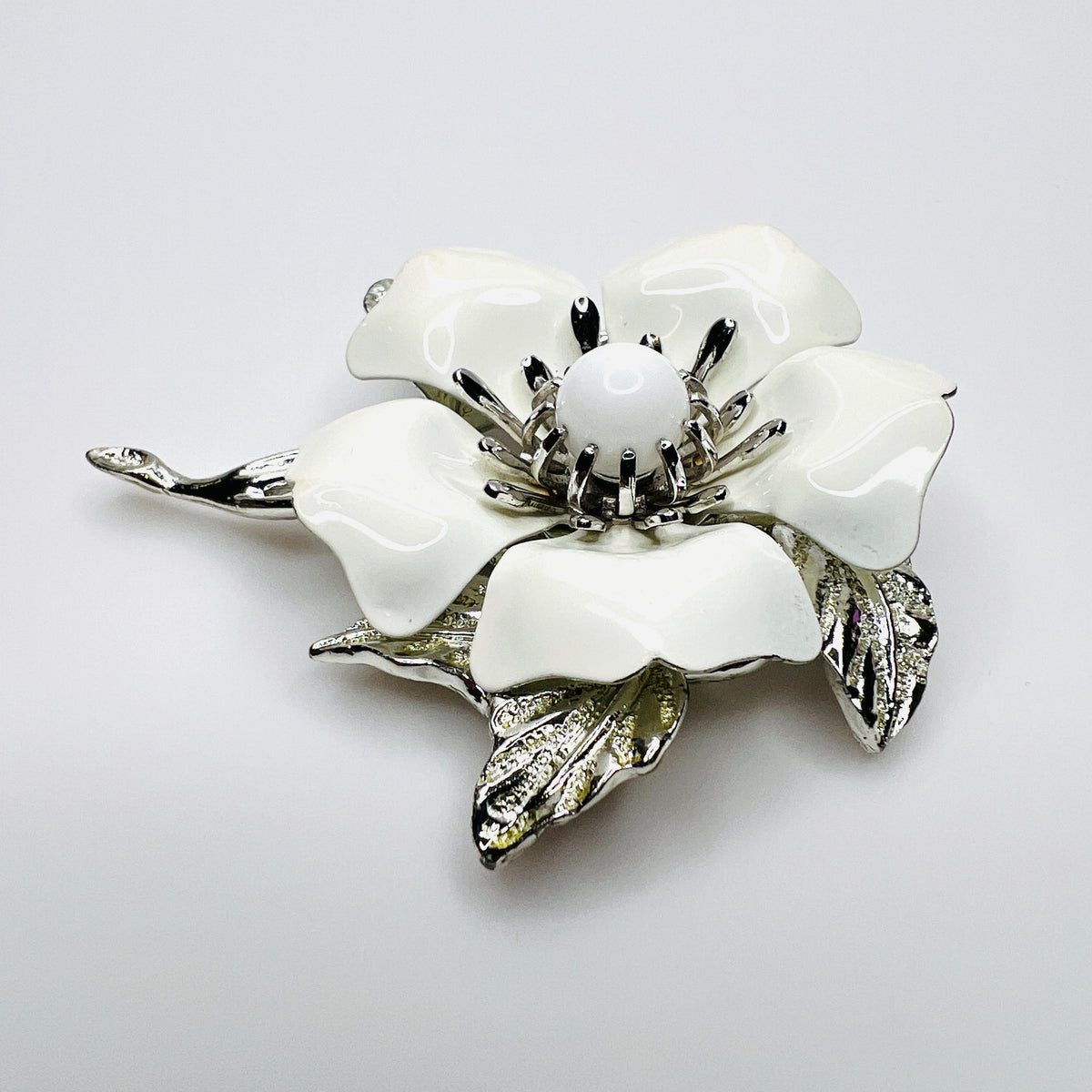 Side view of white enamel flower brooch showing dimensional petals, center and silver-tone leaves