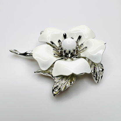 Side view of white enamel flower brooch showing dimensional petals, center and silver-tone leaves