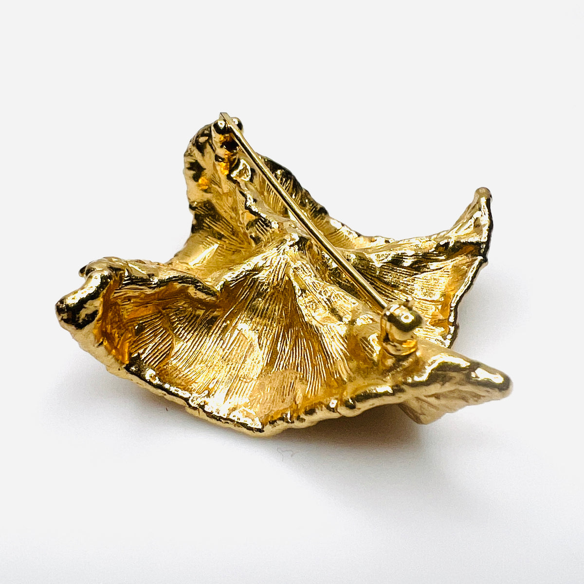 Angled reverse side view of vintage Napier brooch showing deeply sculpted gold-tone folds, dimensional construction, and faux pearl center.