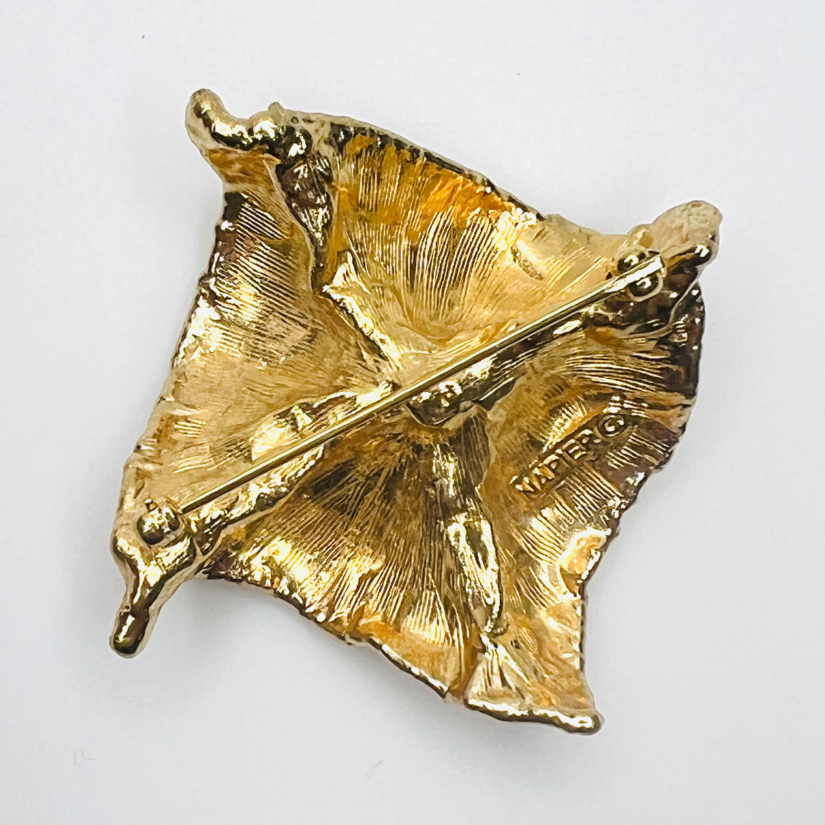 Reverse of vintage 1980s Napier gold-tone brooch showing textured cast-metal backing, rollover safety clasp, and maker's signature.