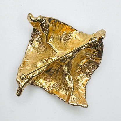 Reverse of vintage 1980s Napier gold-tone brooch showing textured cast-metal backing, rollover safety clasp, and maker's signature.