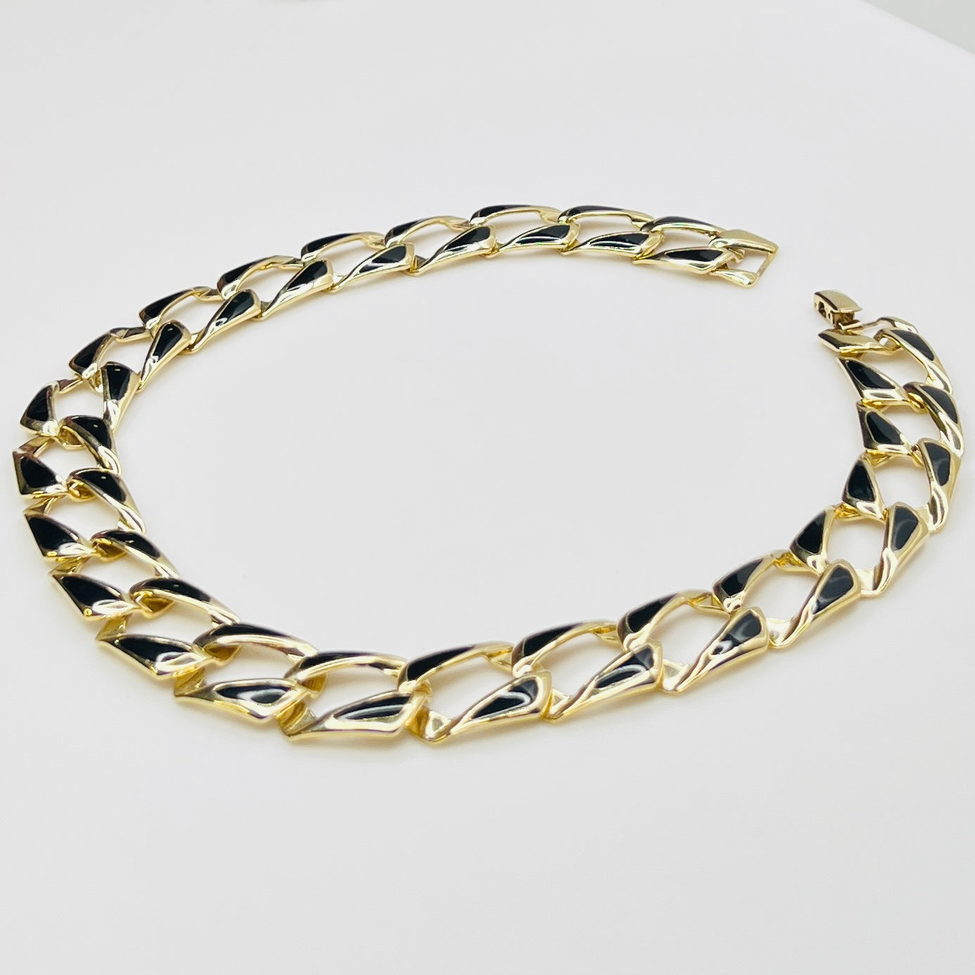Close-up side view of oversized gold tone links with black enamel inlays.