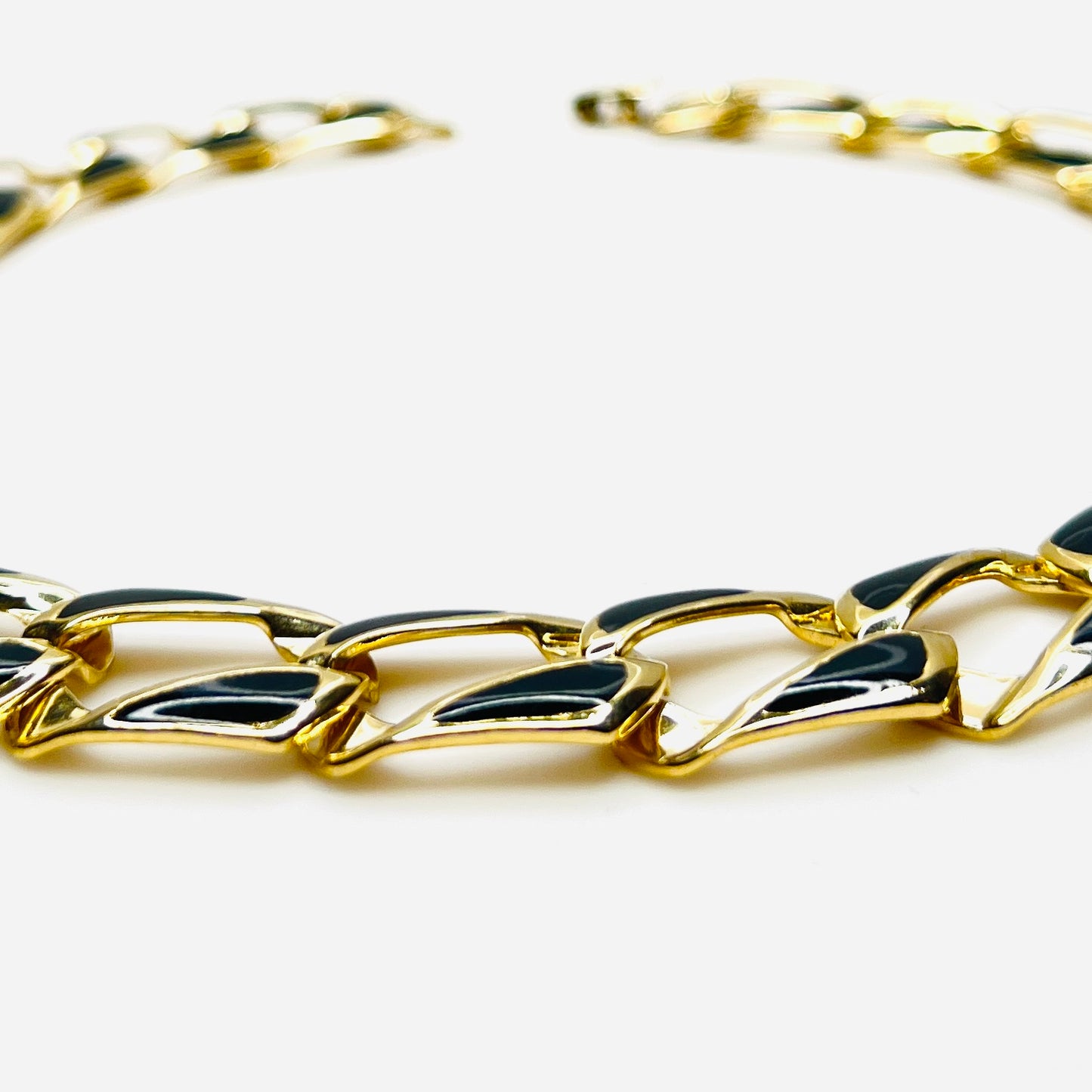 Close-up side view of oversized gold tone links with black enamel inlays.