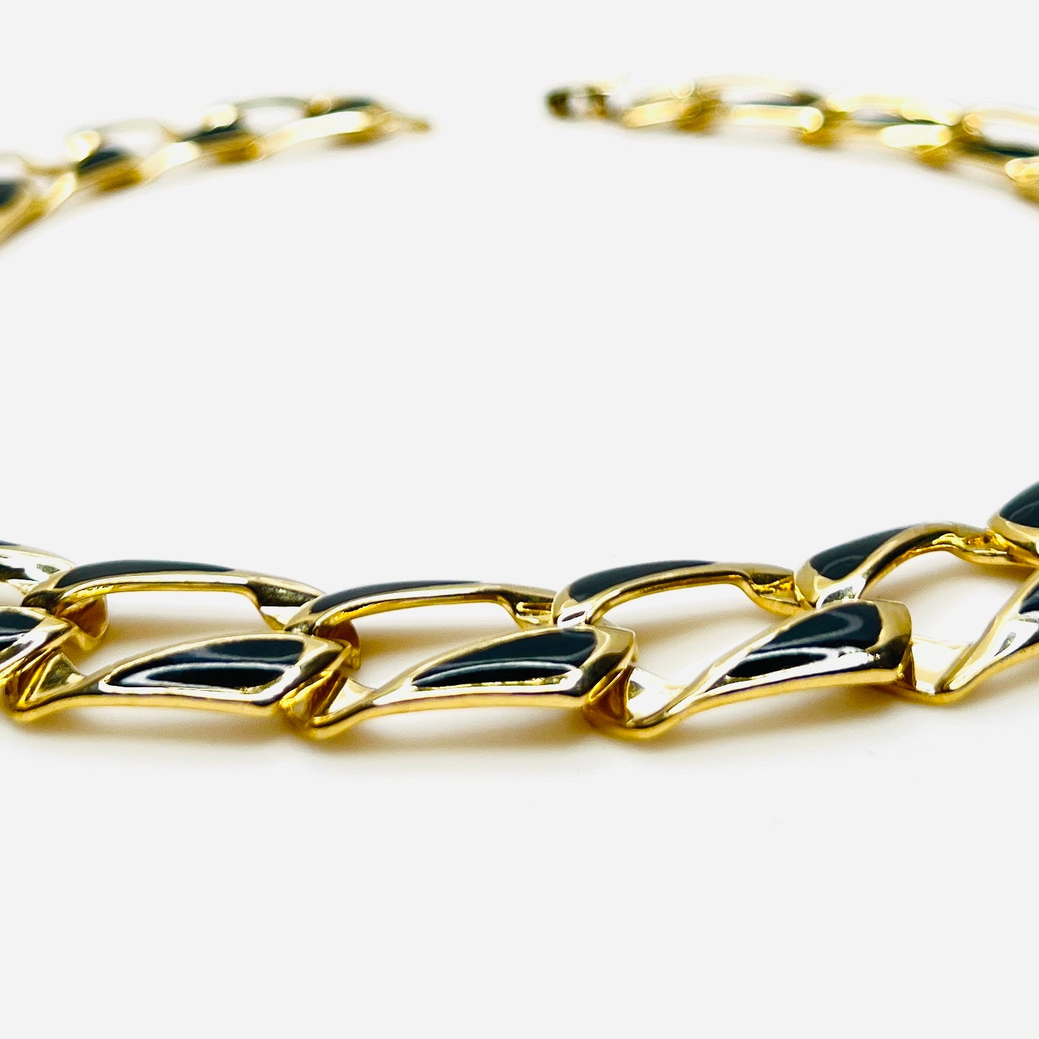 Close-up side view of oversized gold tone links with black enamel inlays.