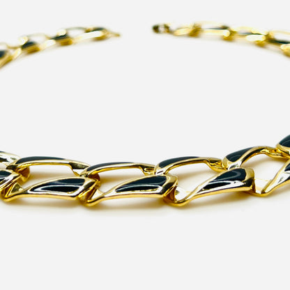 Close-up side view of oversized gold tone links with black enamel inlays.