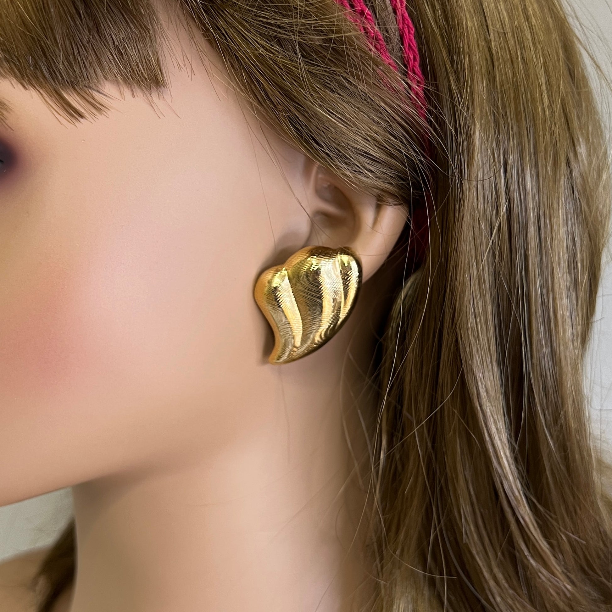 Oversized gold tone abstract wave earrings worn on mannequin ear