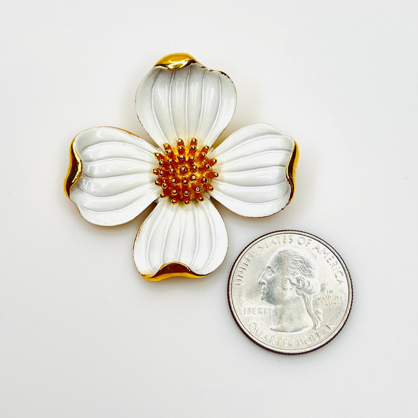 Signed Crown Trifari white enamel floral brooch beside a U.S. quarter for scale.