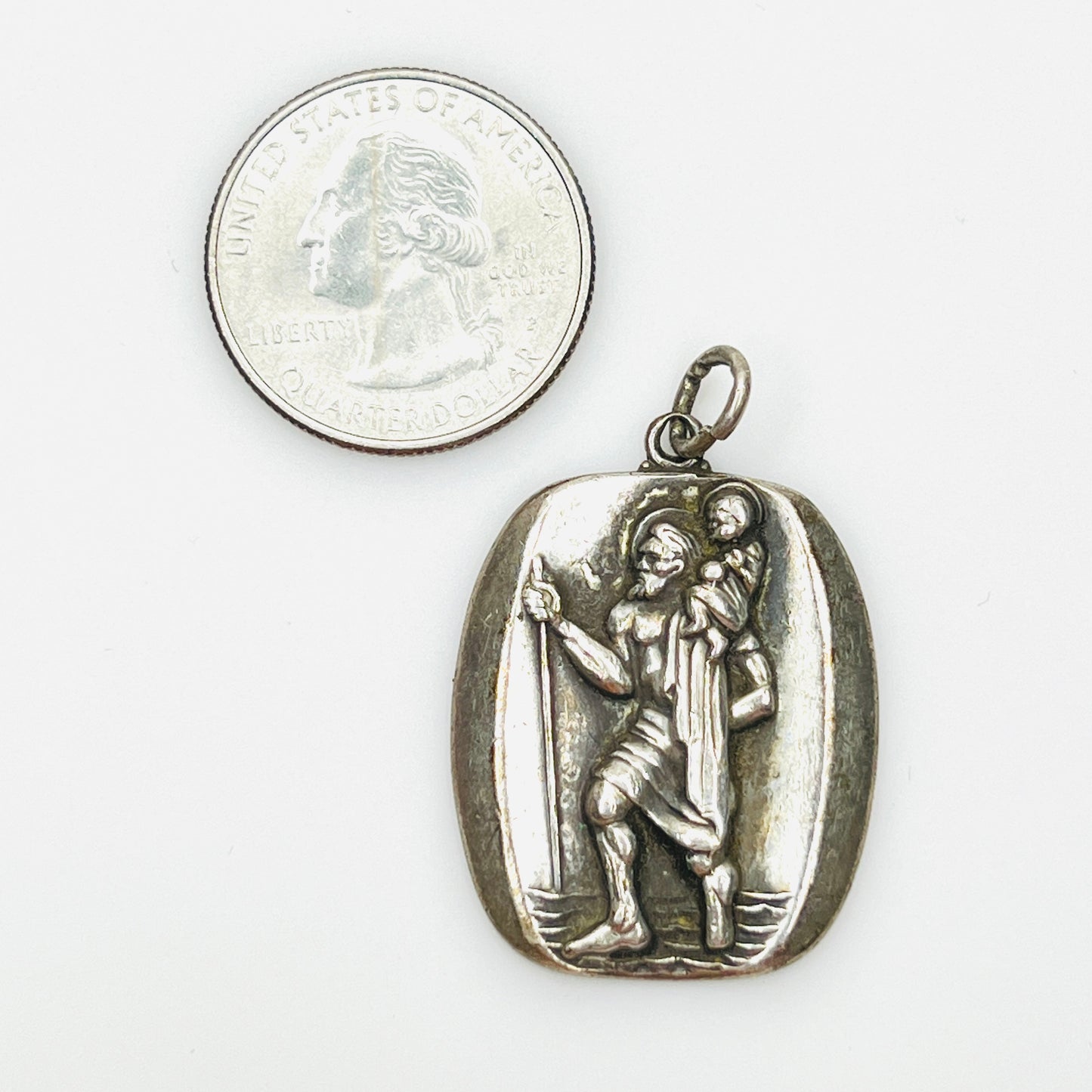 Signed sterling St. Christopher pendant beside quarter showing size and detailed relief.