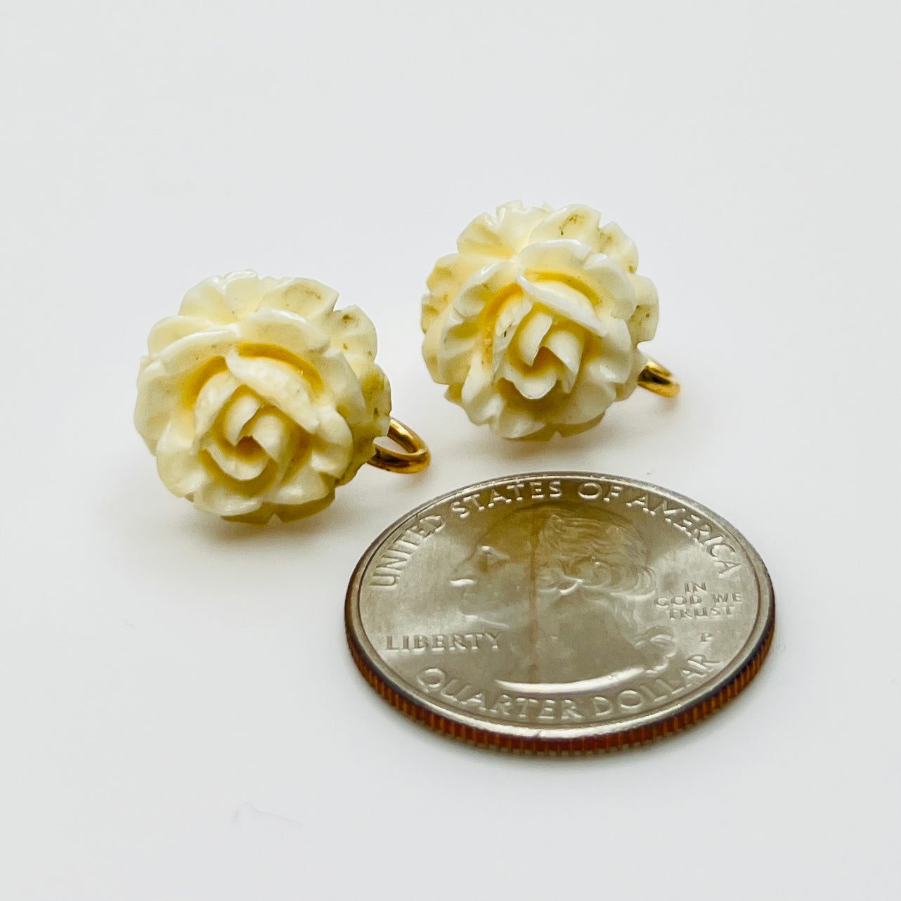 Carved rose earrings next to coin for size reference