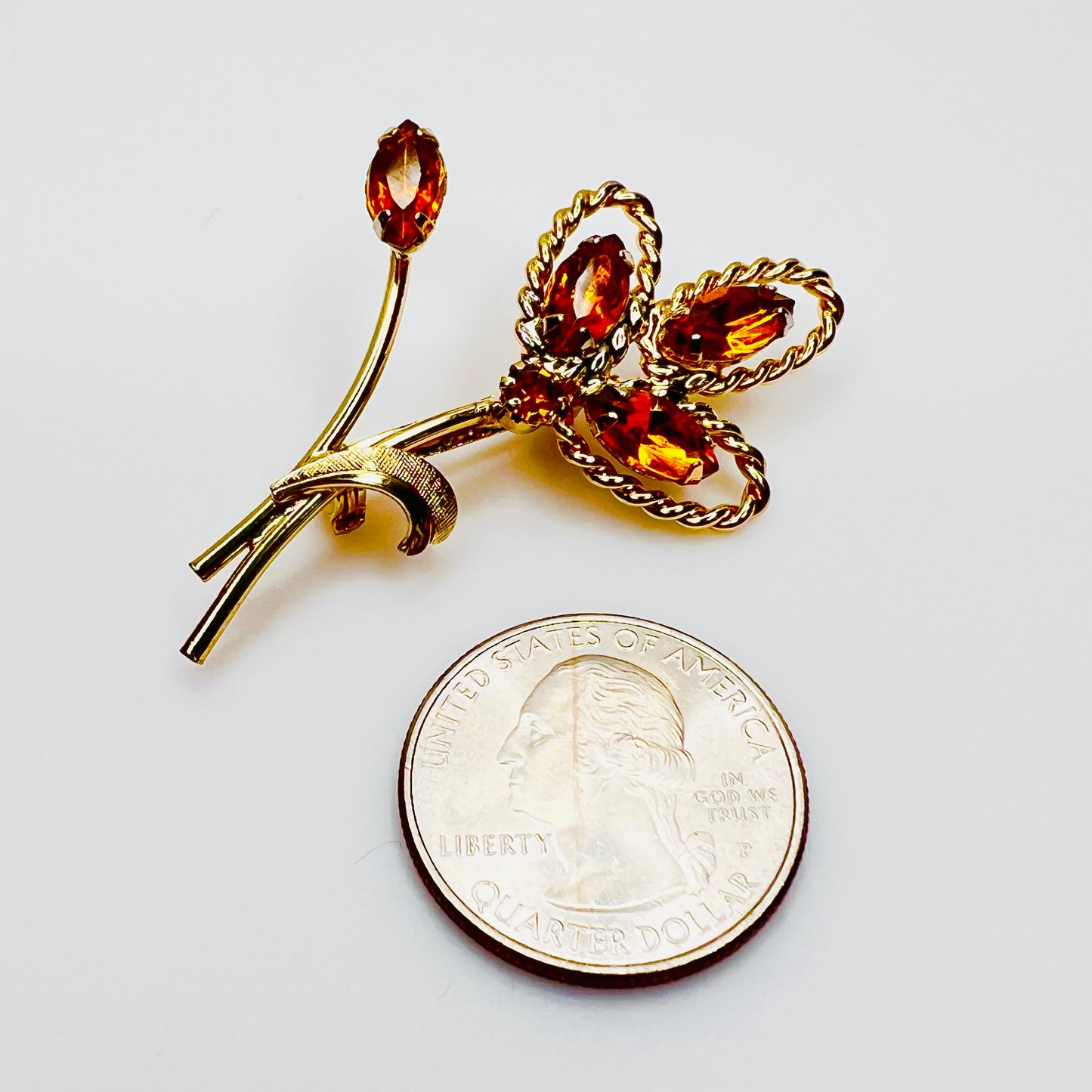 Gold tone floral brooch beside quarter for scale