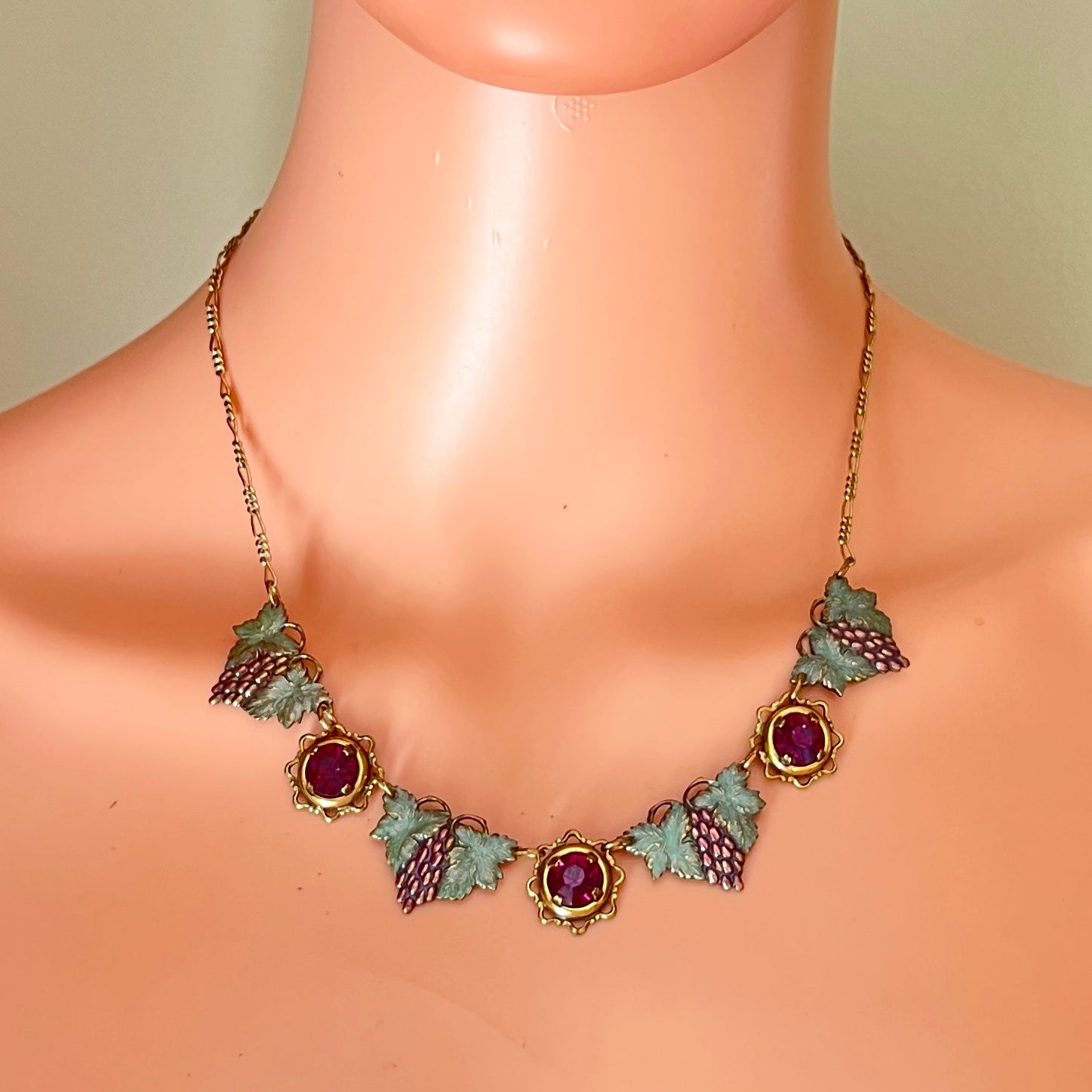 Vintage enamel grape cluster necklace displayed on mannequin with ruby rhinestone accents.